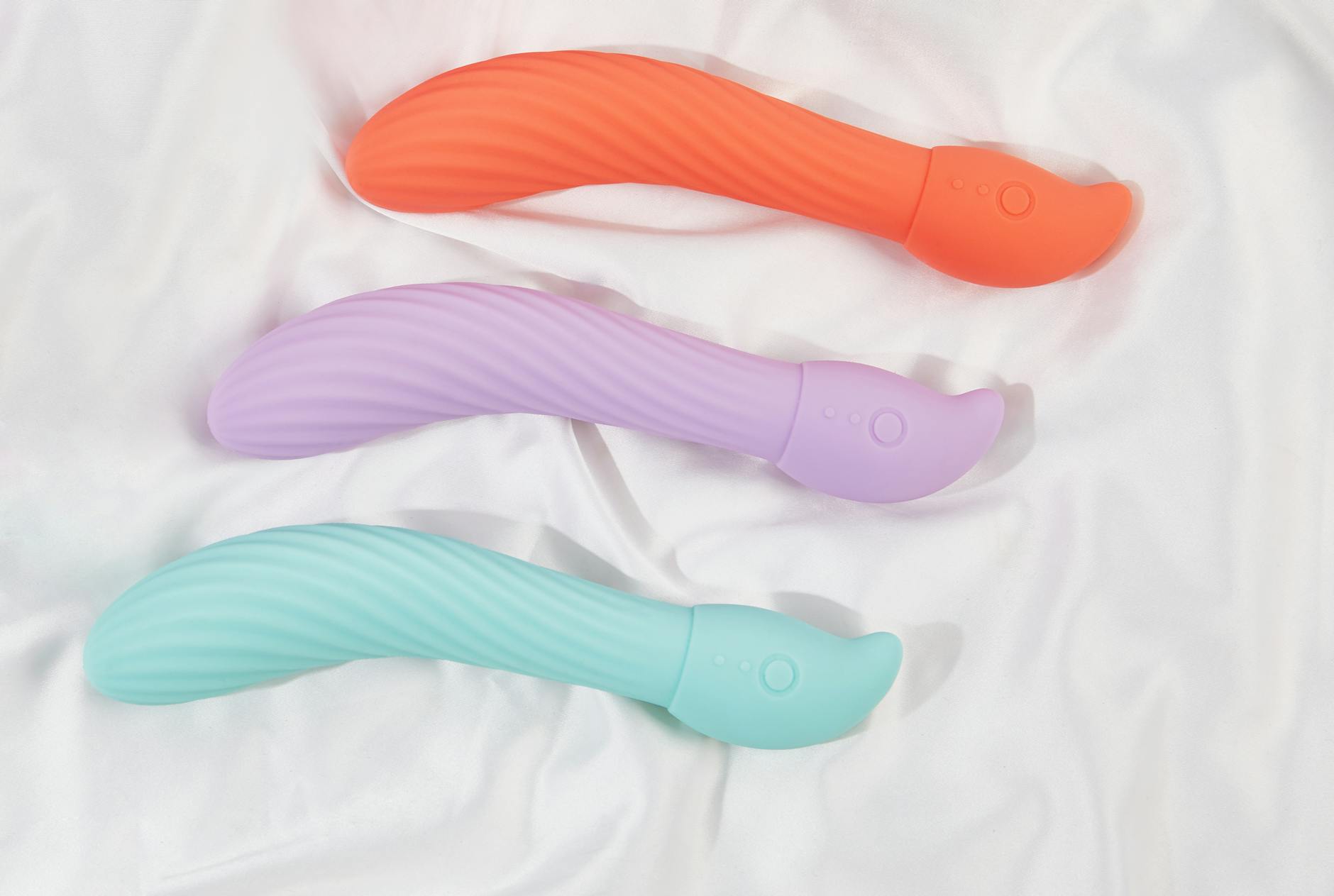 Tre vibratori colorati su tessuto bianco, evidenziando la loro texture liscia