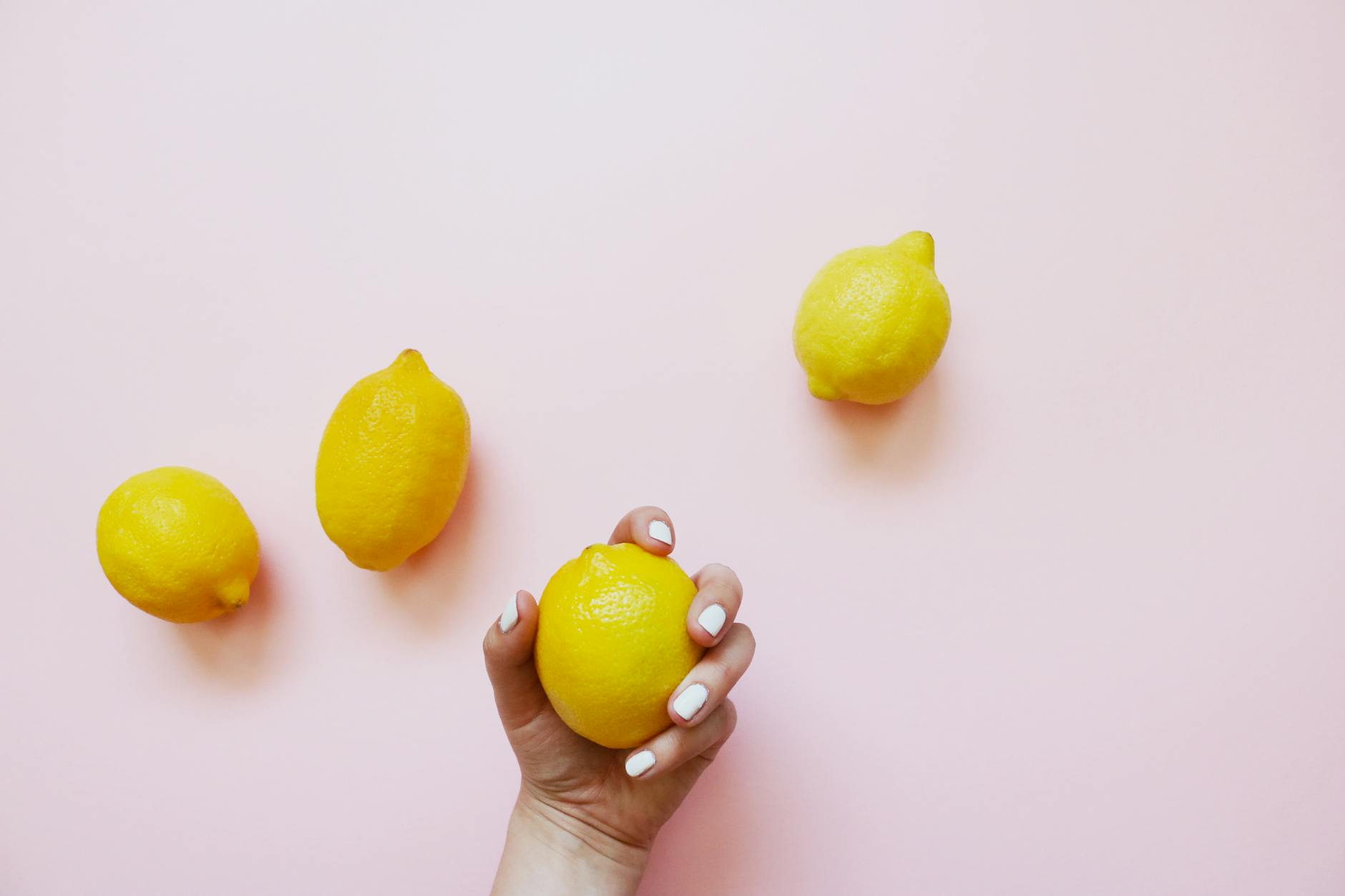 A hand holding a fresh lemon on a soft pink background, symbolizing the design of lemon clitoral vibrators