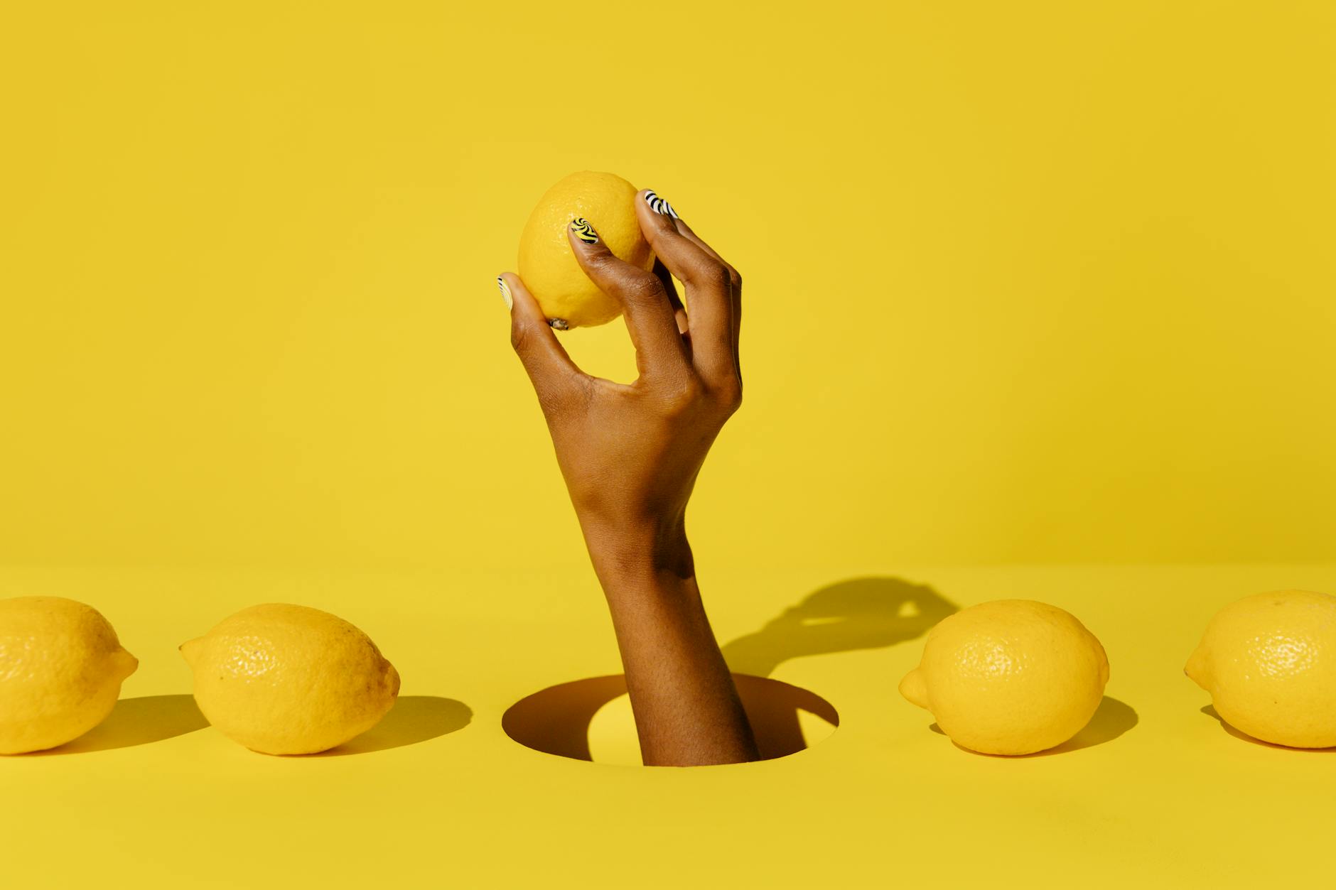 A hand holding a bright lemon against a vivid yellow background, symbolizing freshness and citrus appeal