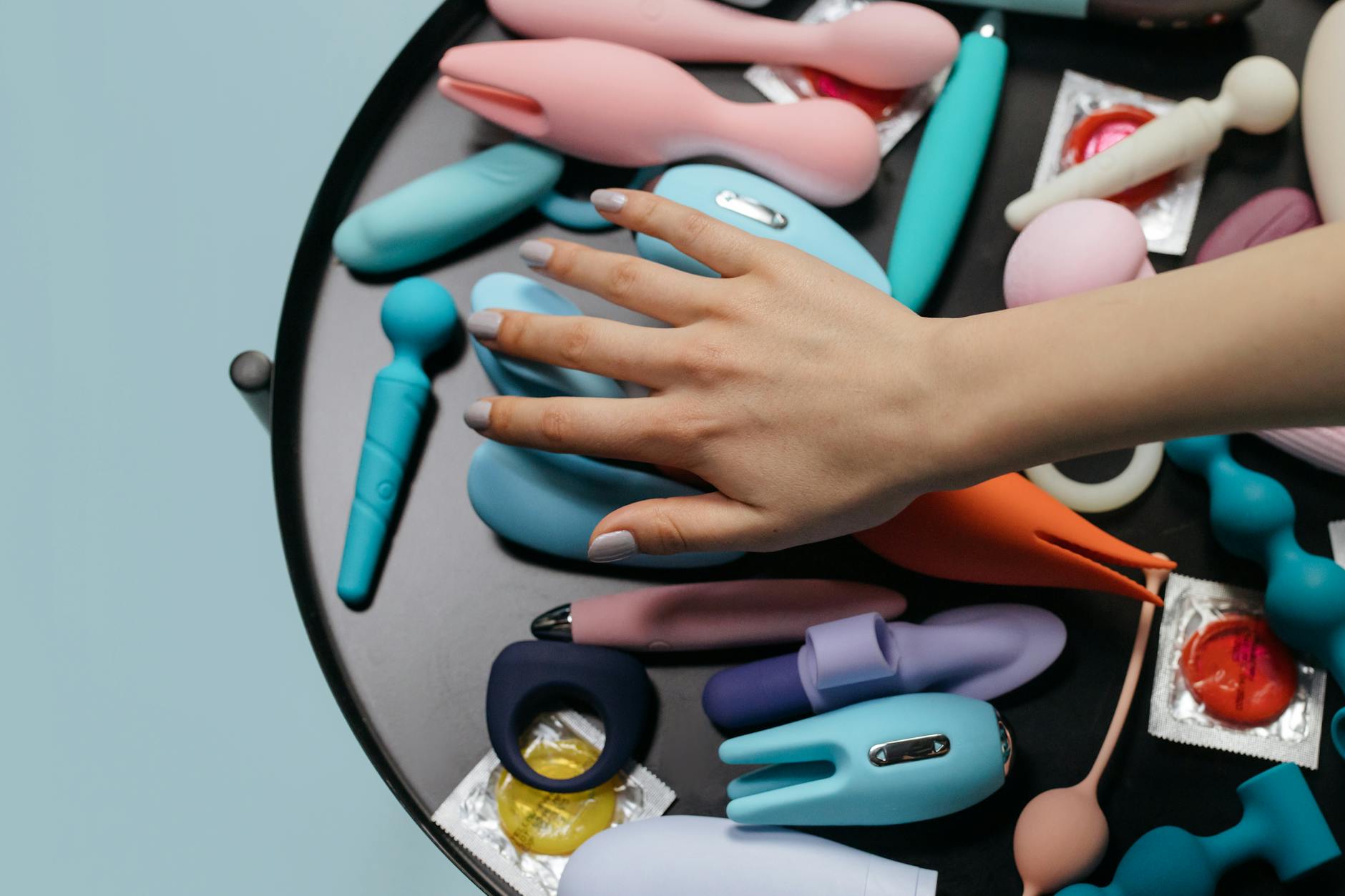 Hand reaching over a variety of colorful sex toys arranged on a minimalist surface