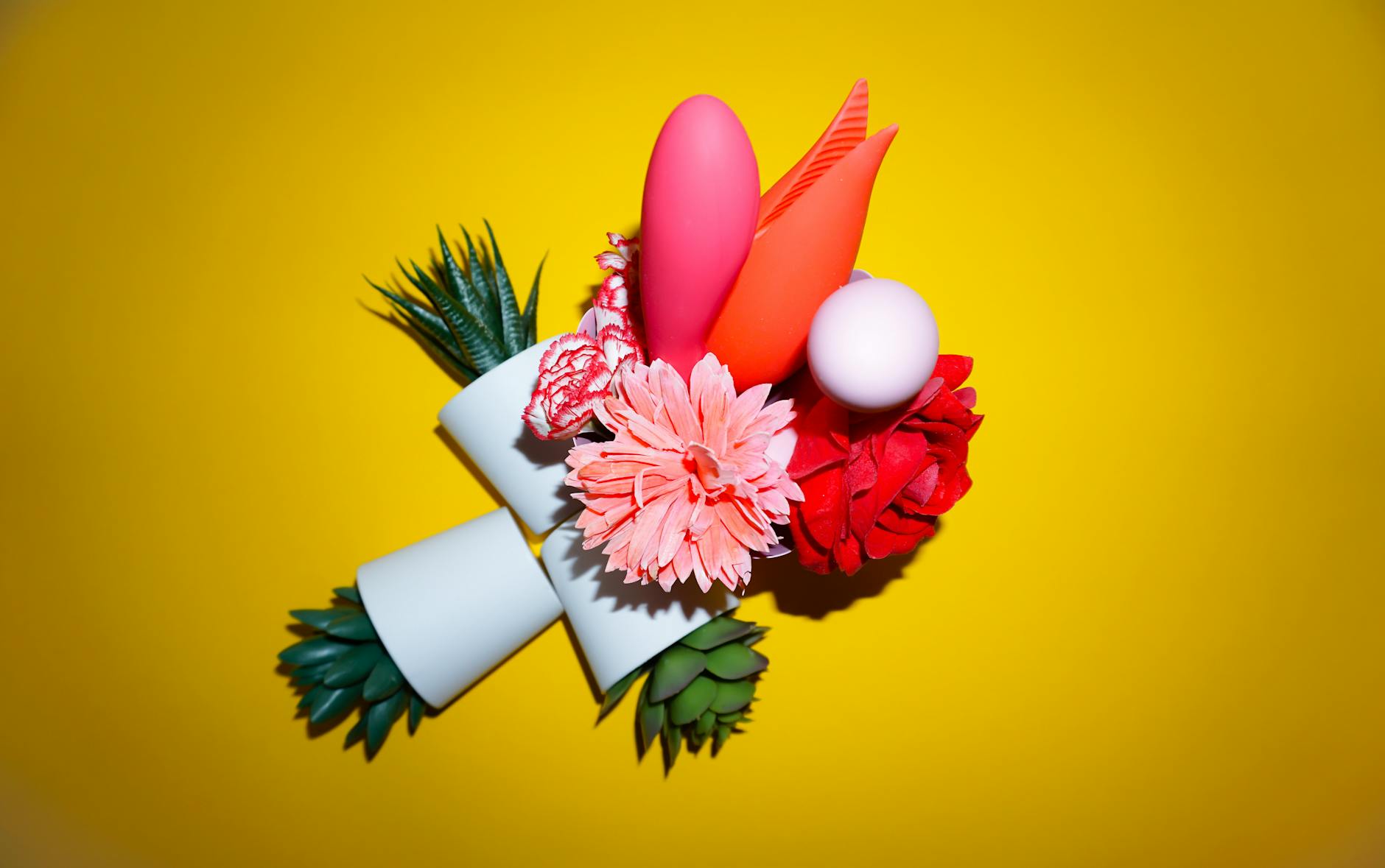 Two hands holding pink and blue silicone clitoral vibrators against a pastel background.